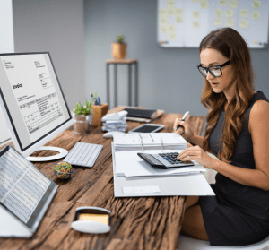 a woman sitting at a desk using a calculator and a computer